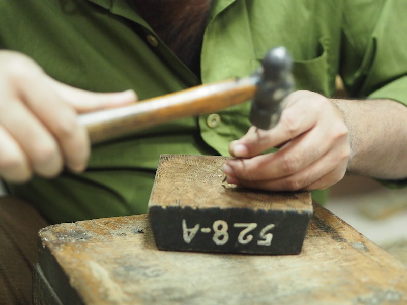 man carving wooden block with nail and hammer